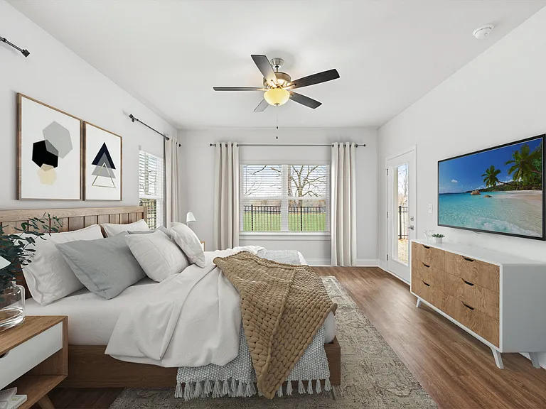 Another perspective view of the serene primary suite, showcasing a modern ceiling fan, sleek entertainment, and sunlit window views.