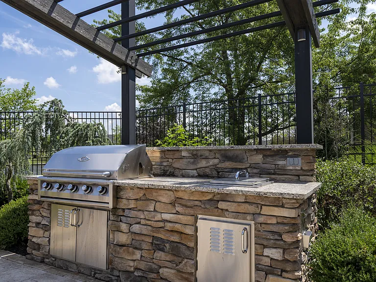 Host unforgettable gatherings in a beautifully designed stone outdoor kitchen, complete with a grill and shaded pergola.