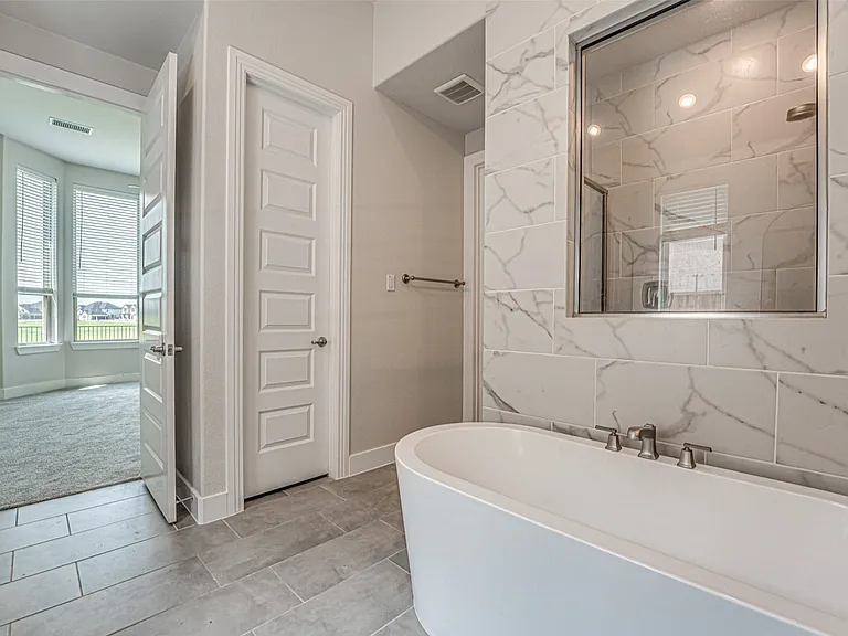Bathroom featuring a freestanding soaking tub, a frameless glass shower enclosure with marbled tile surround, and large format tile flooring