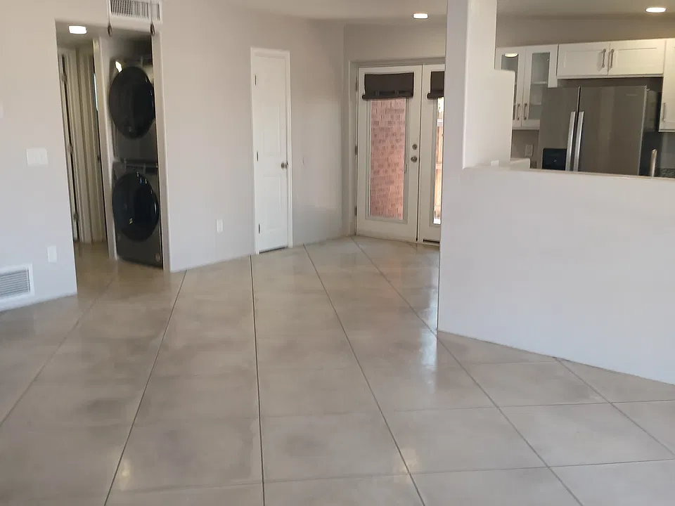 View from front door showing large living room, dining room with French doors going out onto coveredpatio. The floor throughout the unit is concrete overlay in muted gray /beige tones