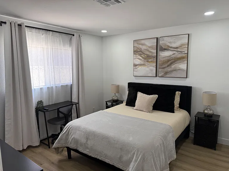 Well-appointed bedroom featuring a comfortable bed, nightstands with lamps, and a dedicated desk area by the window.
