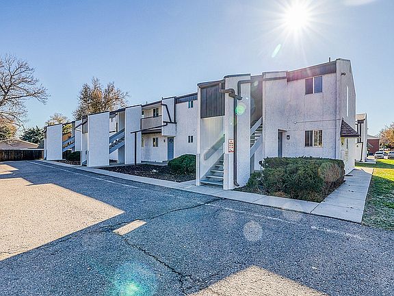 Charming apartment complex with contemporary design, featuring outdoor staircases and lush greenery under a clear, sunny sky.