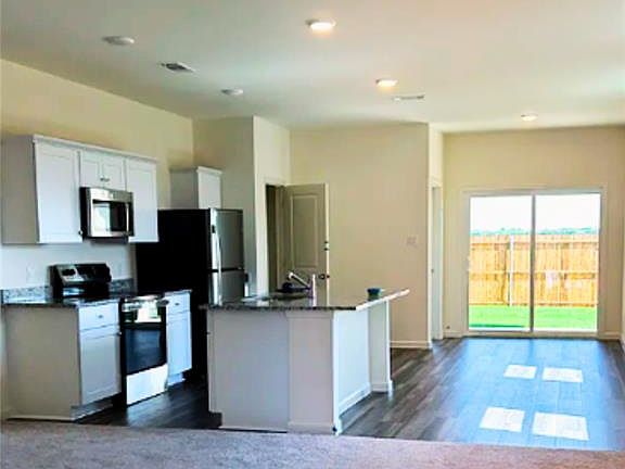 Kitchen featuring open floor plan, stainless steel appliances, white cabinets, a kitchen island, and dark carpet