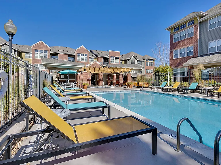 Charming apartment community with a sunlit swimming pool, surrounded by colorful lounge chairs and vibrant modern architecture.