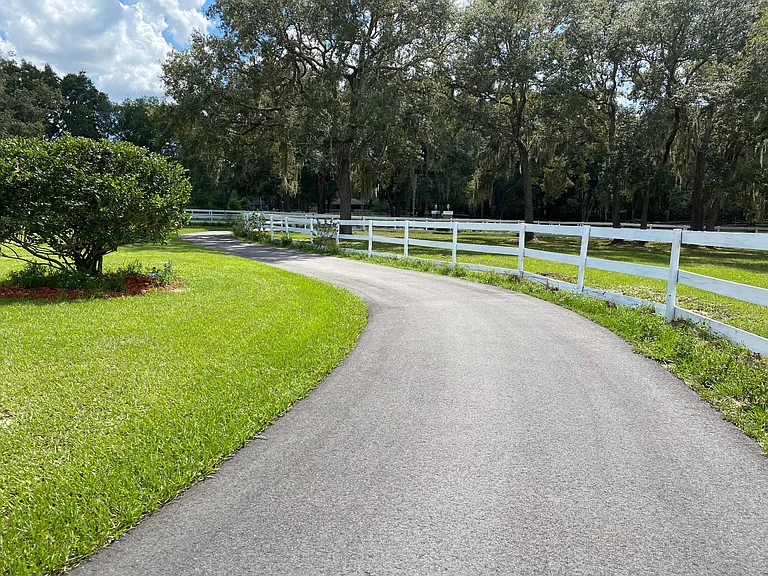 This driveway leads to the front gate of the property. To the left, is the front yard, and to the right, is a paddock.