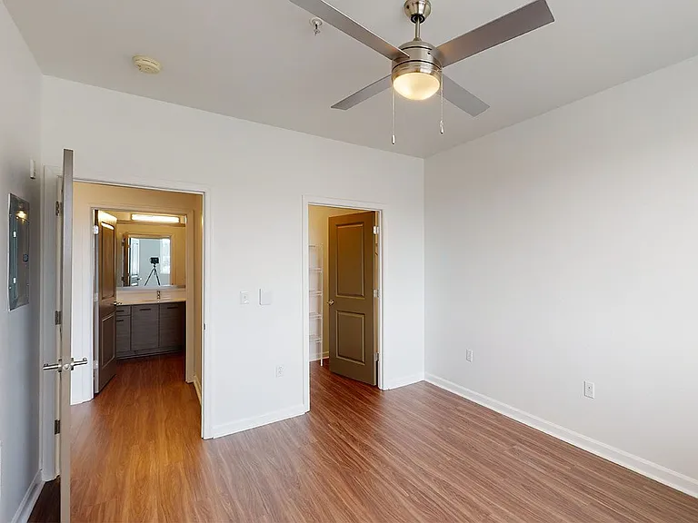 Spacious apartment bedroom with large closet, attached bathroom and wood-style flooring.