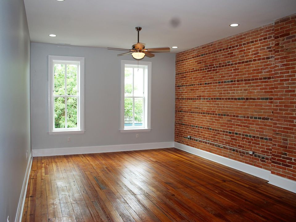 Open-plan living and dining room with original wood floors and exposed brick wall.
