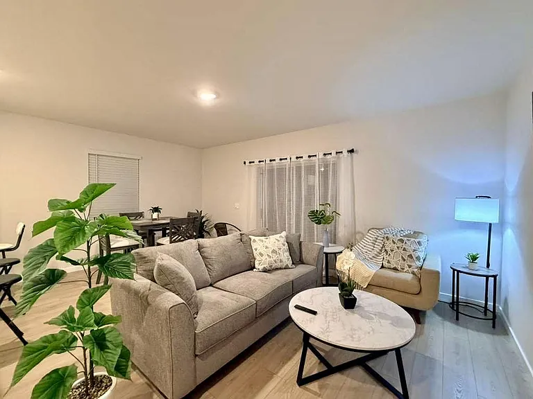 Open living area with sectional seating, accent chair, and coffee table, plus adjacent dining space and window coverings.