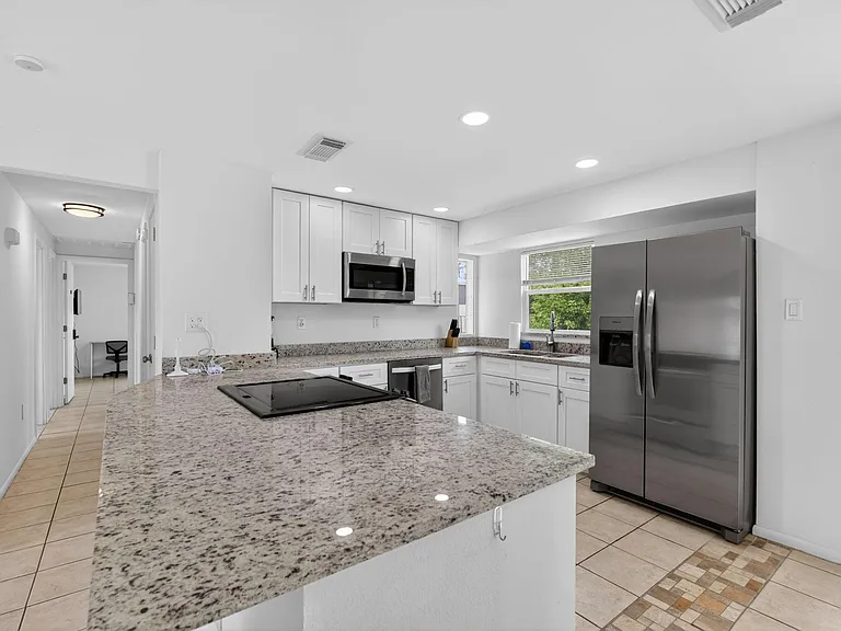 Spacious kitchen with a large granite island, shaker cabinetry, and stainless-steel appliances, plus a window over the sink.