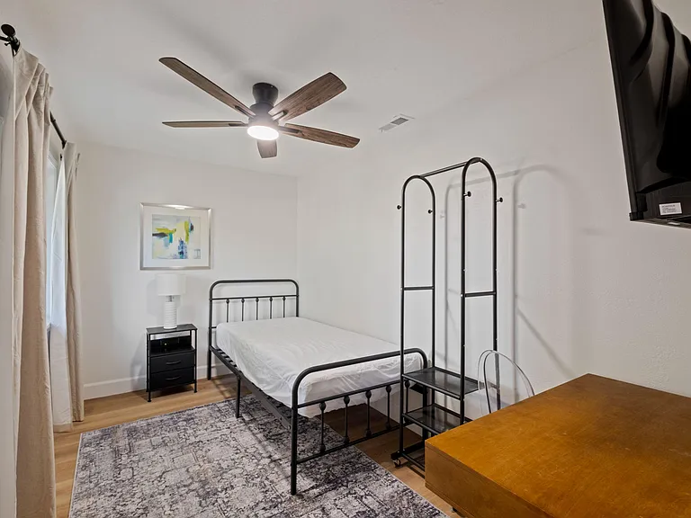 Private bedroom featuring a ceiling fan, window with curtains, bed and nightstand, plus a desk area for work or study.