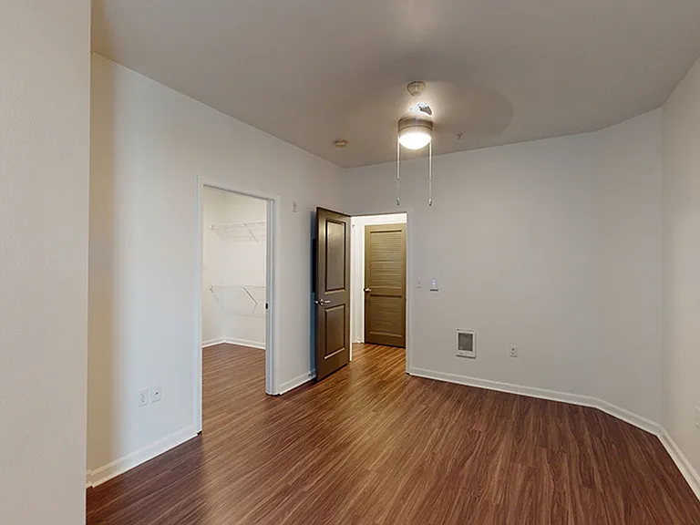 Spacious apartment bedroom with large closet and wood-style flooring.