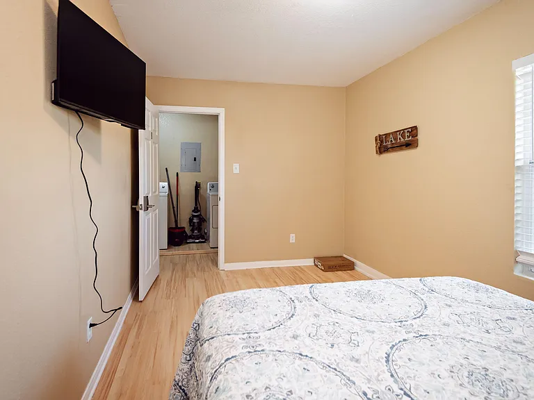 Bedroom with wood-style flooring, a large window with blinds, and wall-mounted TV, plus easy access to the laundry area.