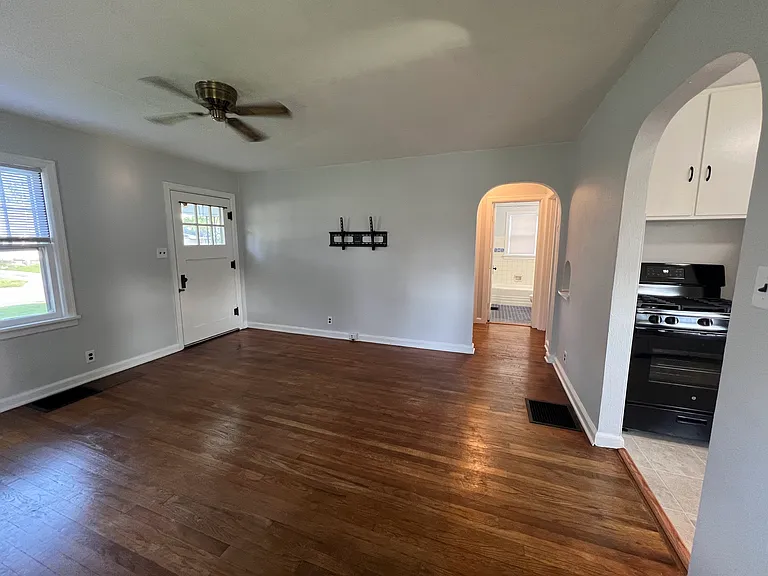 Living room showing the front door, wall mount for TV, and hallway leading to bed and bath rooms.
