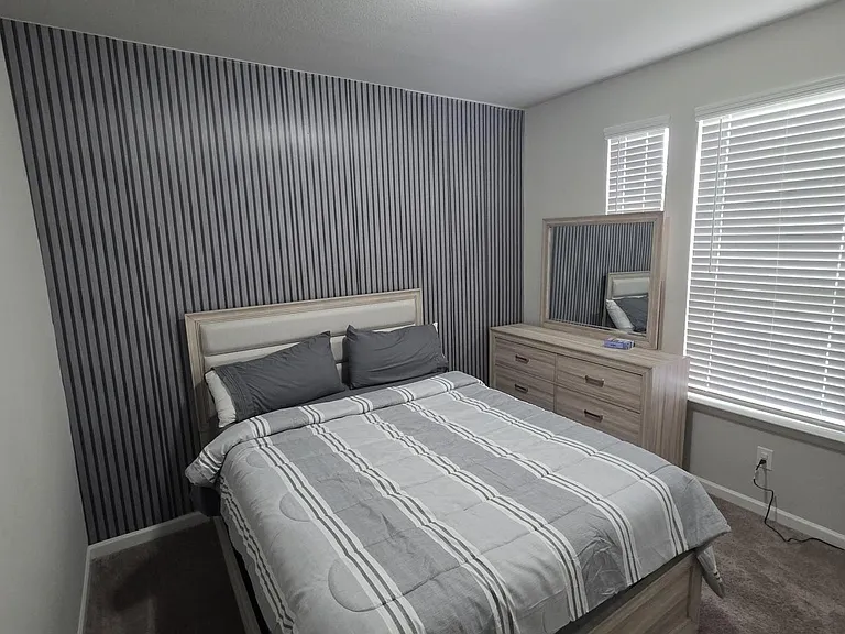 Furnished bedroom with a full bed, matching dresser and mirror, and two windows with blinds for adjustable light.