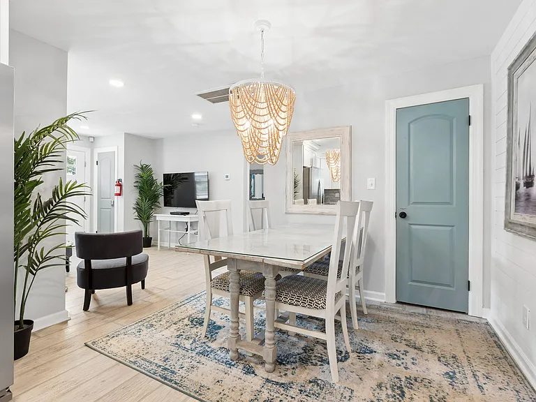 Dining area with a glass-top table for four, statement chandelier, and open flow to the kitchen and living space.