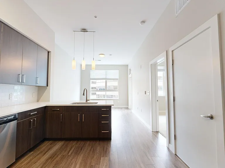 Apartment kitchen with stainless steel appliances, dining and living room with wood-style flooring.