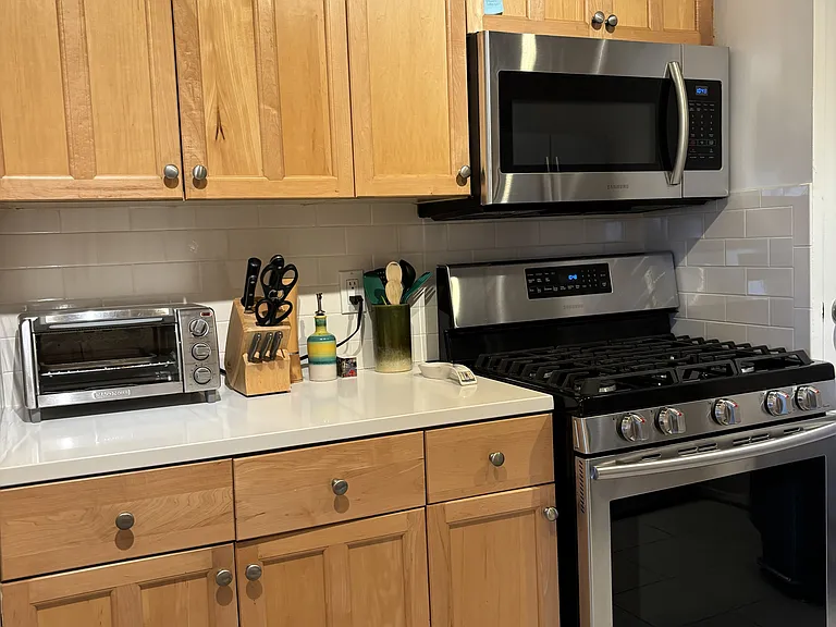 Kitchen, view to the left side when you enter. Black and Decker toaster oven, with Samsung gas range stove and oven, and Samsung microwave, with ample cabinets filled with kitchen essentials and more.