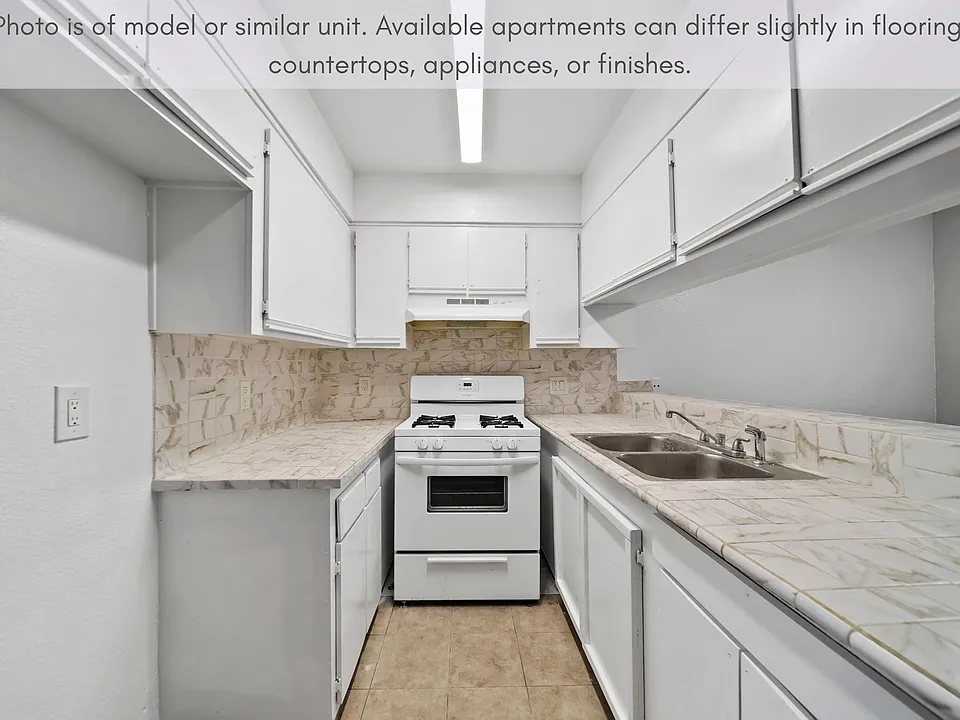 Galley-style kitchen featuring generous cabinet space, tiled countertops, and a gas range.