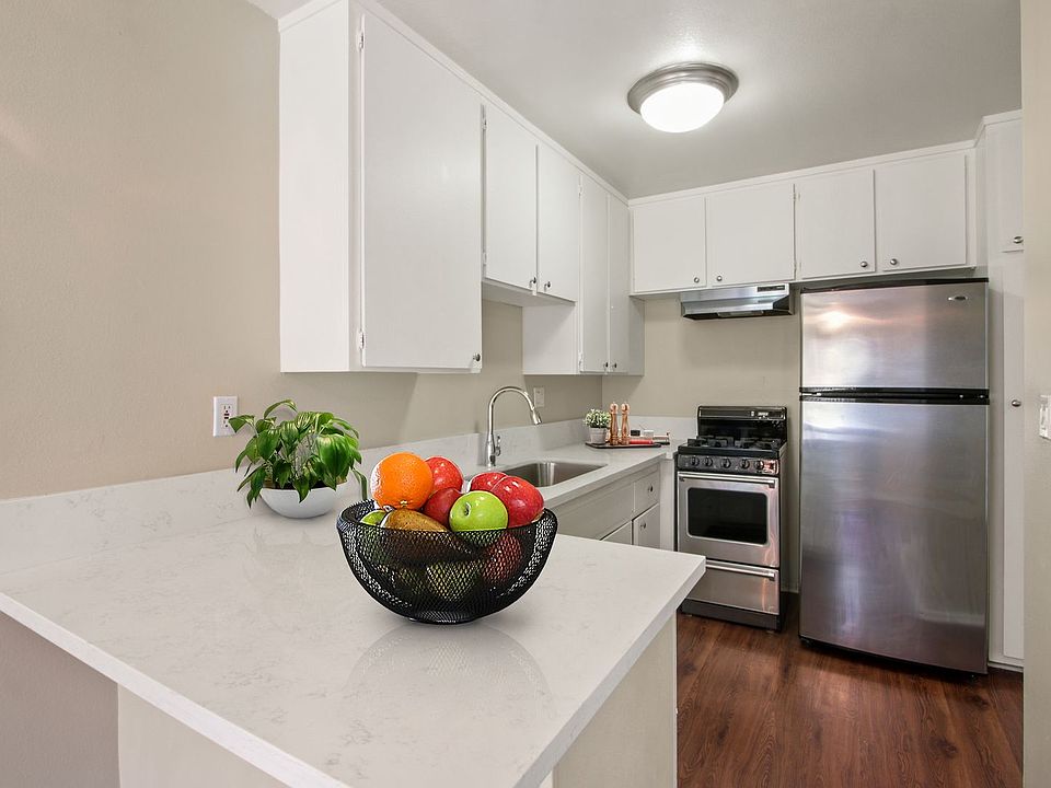 Kitchen with stainless steel two-door refrigerator, gas stove over range hood, white cabinets, quartz counter tops
