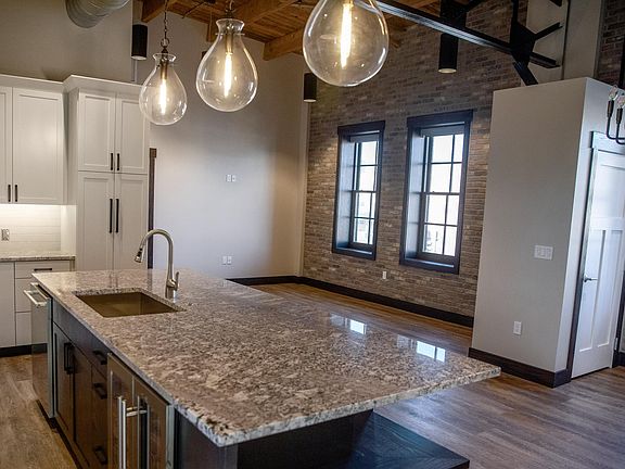 Open concept view from kitchen to living room space. Exposed brick, ceilings.