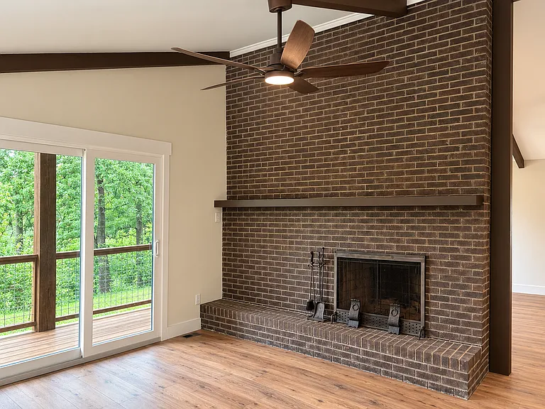 A spacious living room showcases a vaulted ceiling with beam details, a second floor-to-ceiling brick fireplace, and sliding glass doors that open to the deck, creating a seamless connection between indoor comfort and breathtaking outdoor views.