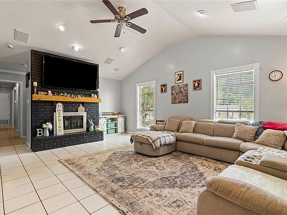 Living room featuring light tile patterned flooring, vaulted ceiling, visible vents, a ceiling fan, and a fireplace