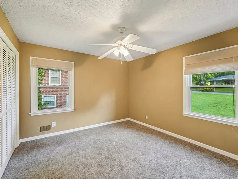 This charming bedroom feels calm and inviting, with a sweet window view, plush carpeting, and a ceiling fan that adds everyday comfort with storybook simplicity.