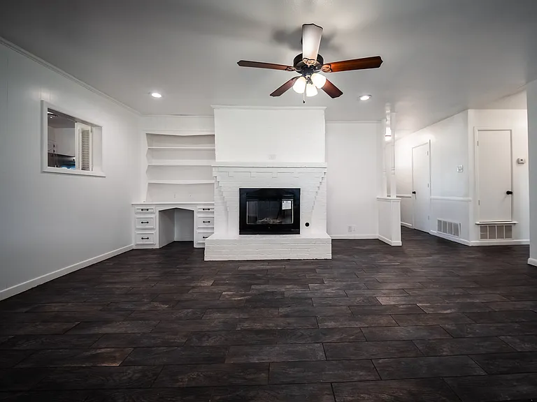 Spacious living room with ceiling fan, hardwood floors, and cozy fireplace