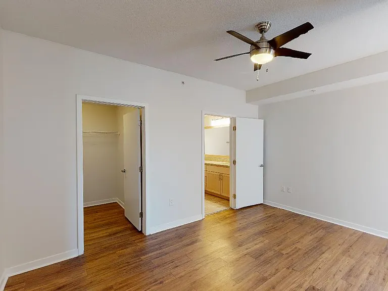 Spacious apartment bedroom with large closet, attached bathroom and wood-style flooring.