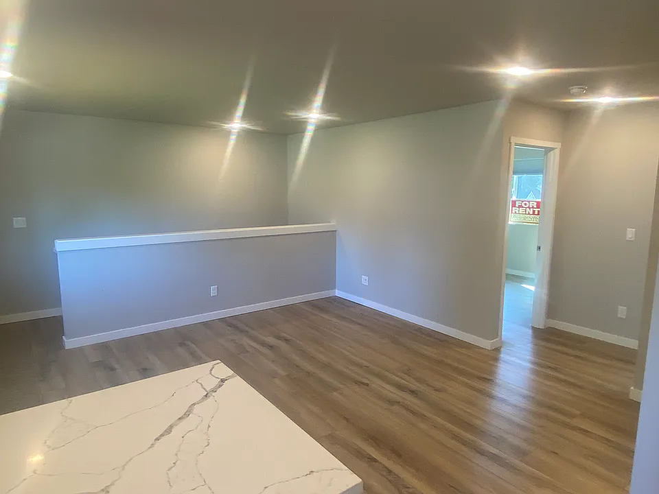 View from kitchen shows living room area and faux wood floors. Well lit area highlights colors that also tie into floor colors.
