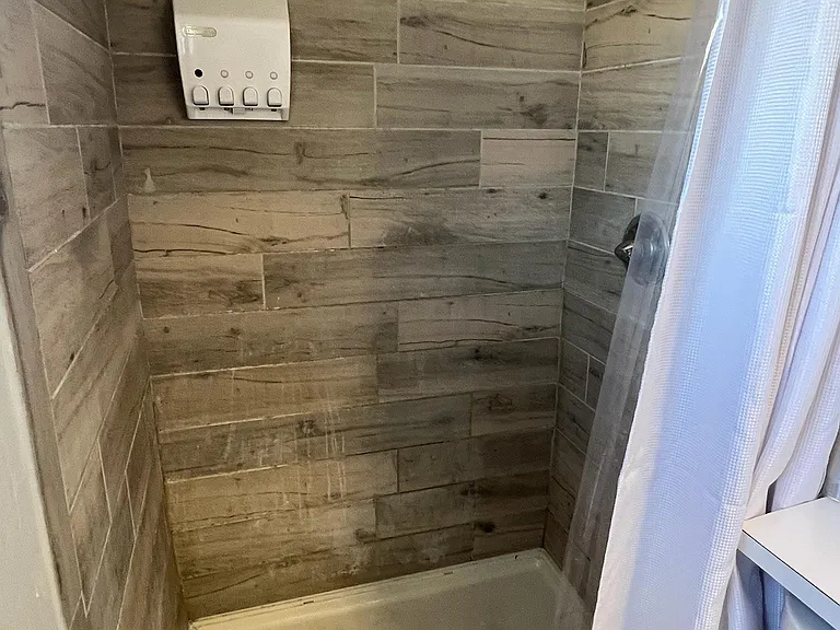Tub/shower combo with wood-look tile surround, overhead showerhead, and included curtain for easy daily use.