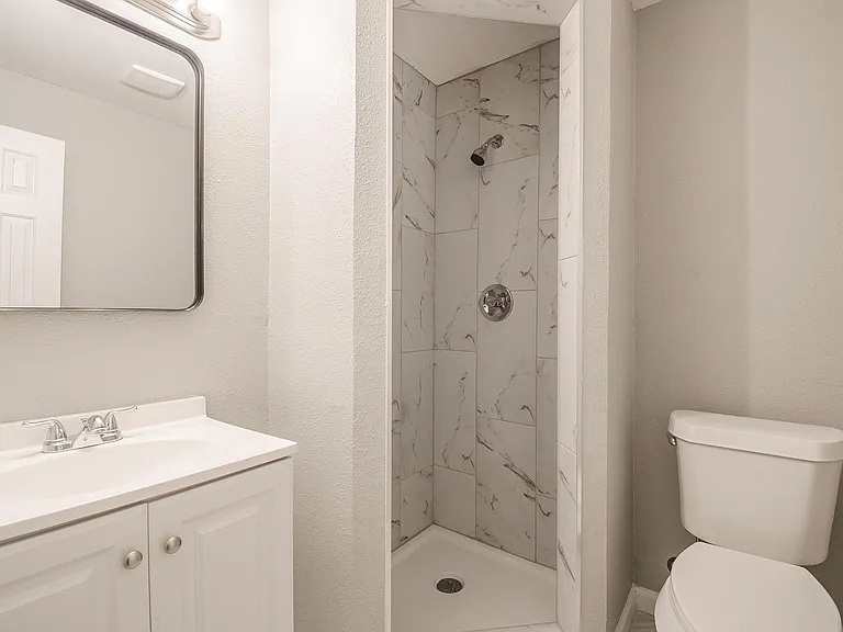 Clean full bathroom with a vanity and mirror plus a tiled walk-in shower and updated fixtures for everyday convenience.