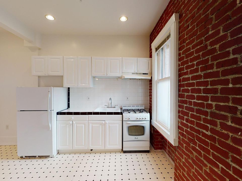 Kitchen with multiple cabinets, refrigerator, stove, range hood, and sink