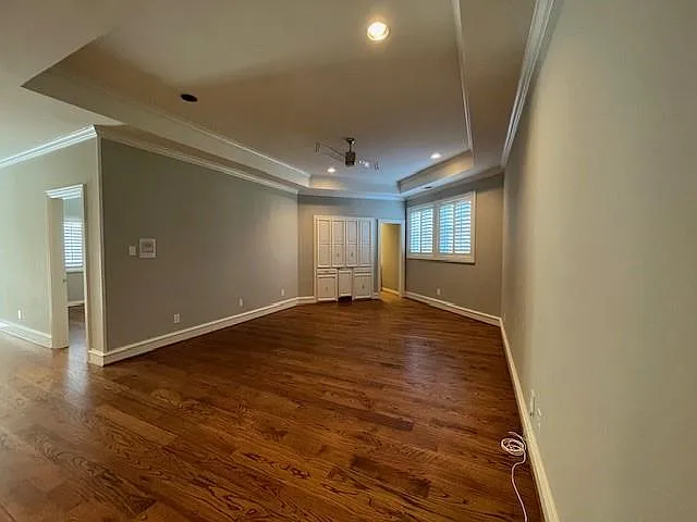 Empty room with ornamental molding, dark wood-type flooring, recessed lighting, and a tray ceiling