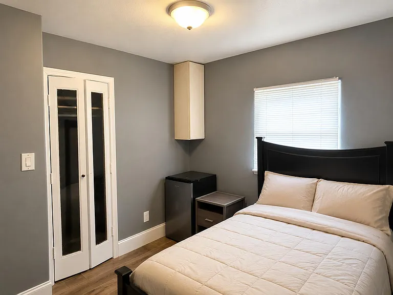 Furnished bedroom with a comfortable bed, bedside table, mini fridge, and a closet for convenient storage.