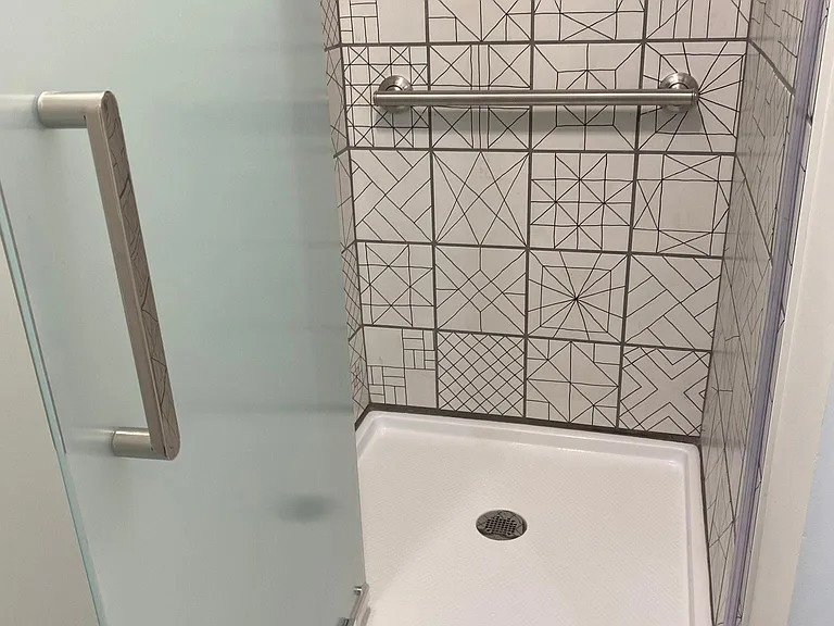 STUNNING white and black tile shower with stainless steel grab bar, matte black shower head and single lever controller.