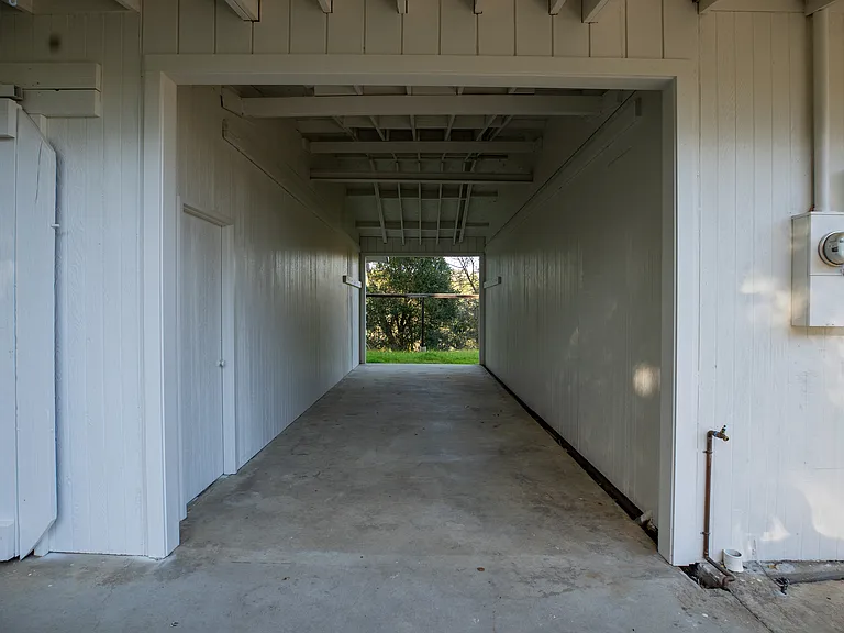 A unique covered outdoor hallway behind the rear bedroom will inspire you to decorate and use this space. Could be an outdoor bar or private storage. To the left is extra storage with sliding barn doors. A great spot to put your toys or equipment.