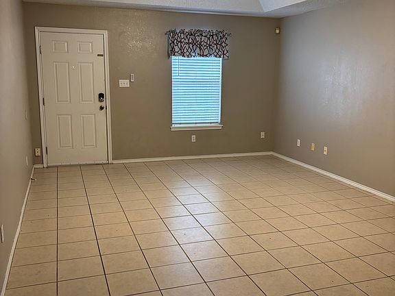 Living Room with ceiling fan in vaulted ceiling and decorative curtain and rod that stays for tenant use. Window has one inch Levolor blinds. Easy to clean tile floors throughout the apartment.