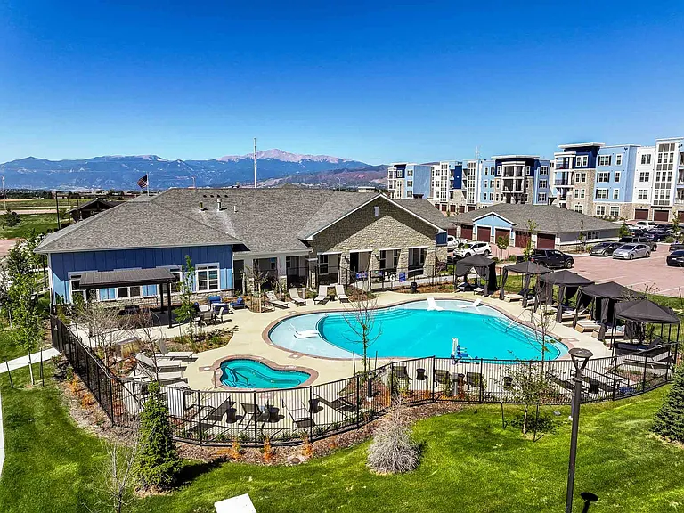 The resort-style pool and attached spa at The Baldwin Modern Apartments, framed by a sundeck of loungers, private cabanas, and sweeping views of Pikes Peak and the Front Range in northern Colorado Springs.