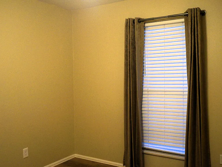 Den has thermal blackout curtains with white faux wood blinds.