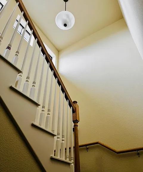 Staircase detail featuring wood banister, decorative pendant light, and three windows bringing in plenty of natural light