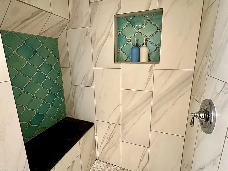 Beautiful walk-in shower featuring handcrafted ceramic tile, a built-in stone bench with natural fossils, and a recessed niche for shampoo and soap storage