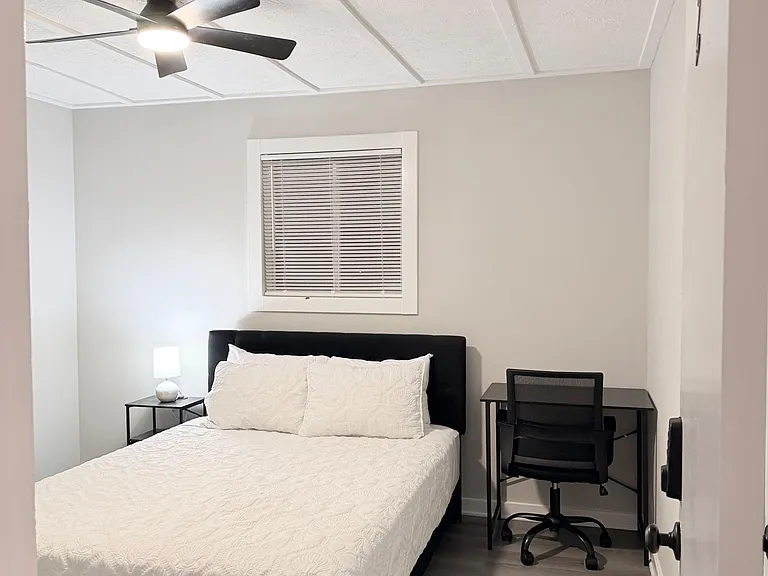 Furnished bedroom with a full bed, ceiling fan, and a dedicated desk workspace for studying or remote work.