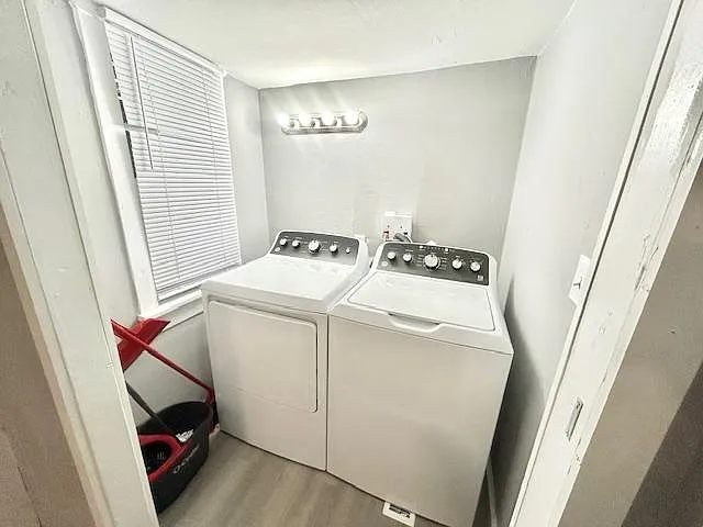 Dedicated laundry nook with side-by-side washer and dryer, overhead lighting, and a window for ventilation.