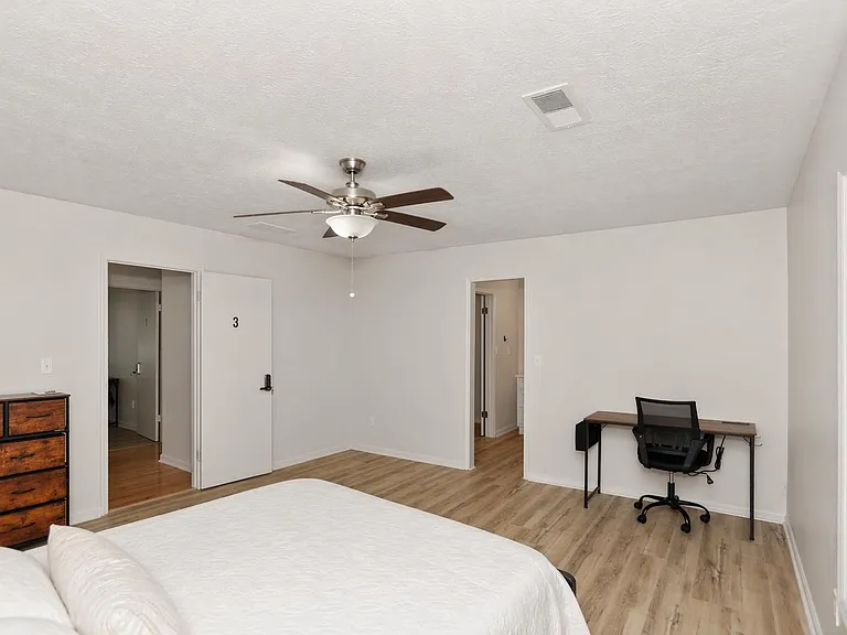 Spacious bedroom with wood-look flooring, ceiling fan, and a dedicated desk areaideal for work or study.