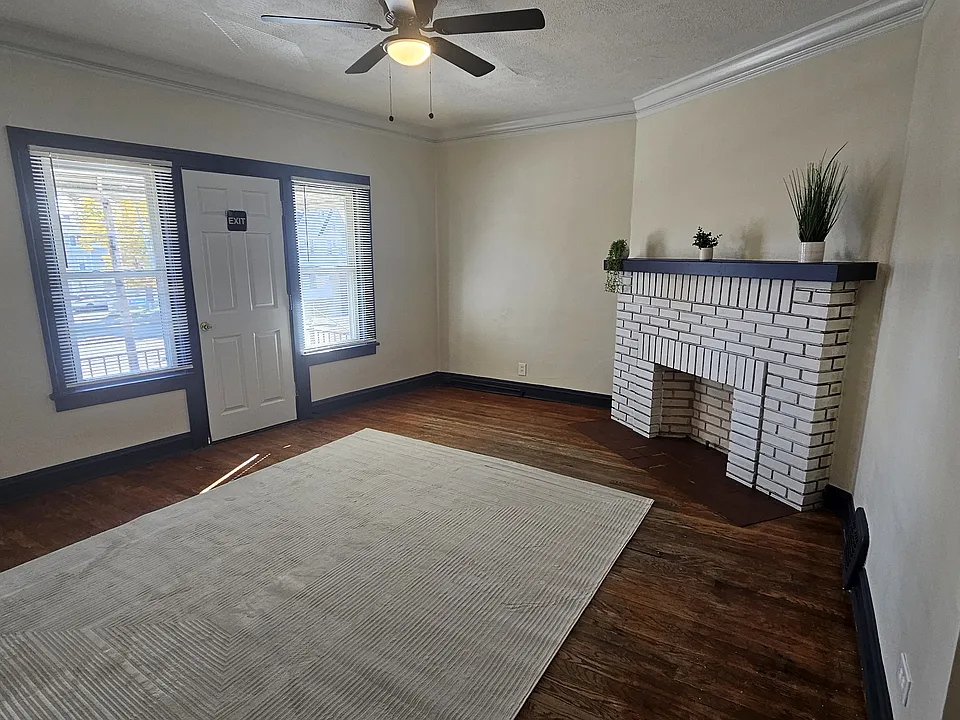 Freshly-painted living room with fireplace, new fan, new blinds, and balcony access.