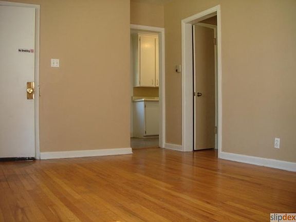 From the living room, you see the kitchen entrance with the white cabinets and the bathroom/bedroom door on the right.