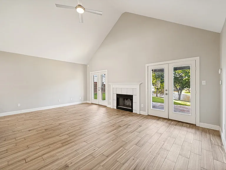Vaulted ceiling great room featuring wood-finish flooring, a fireplace with a white mantel and tile surround, and dual pane French doors opening to the exterior