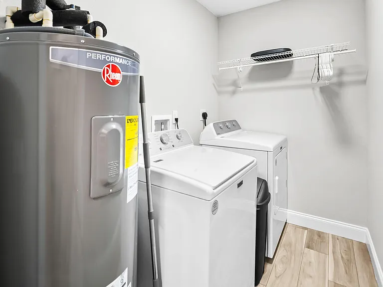 Dedicated laundry area with full-size washer and dryer, plus a wall-mounted shelf and hanging rod for added storage.