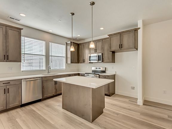 Modern kitchen with wooden cabinets, island, stainless steel appliances, and two pendant lights.